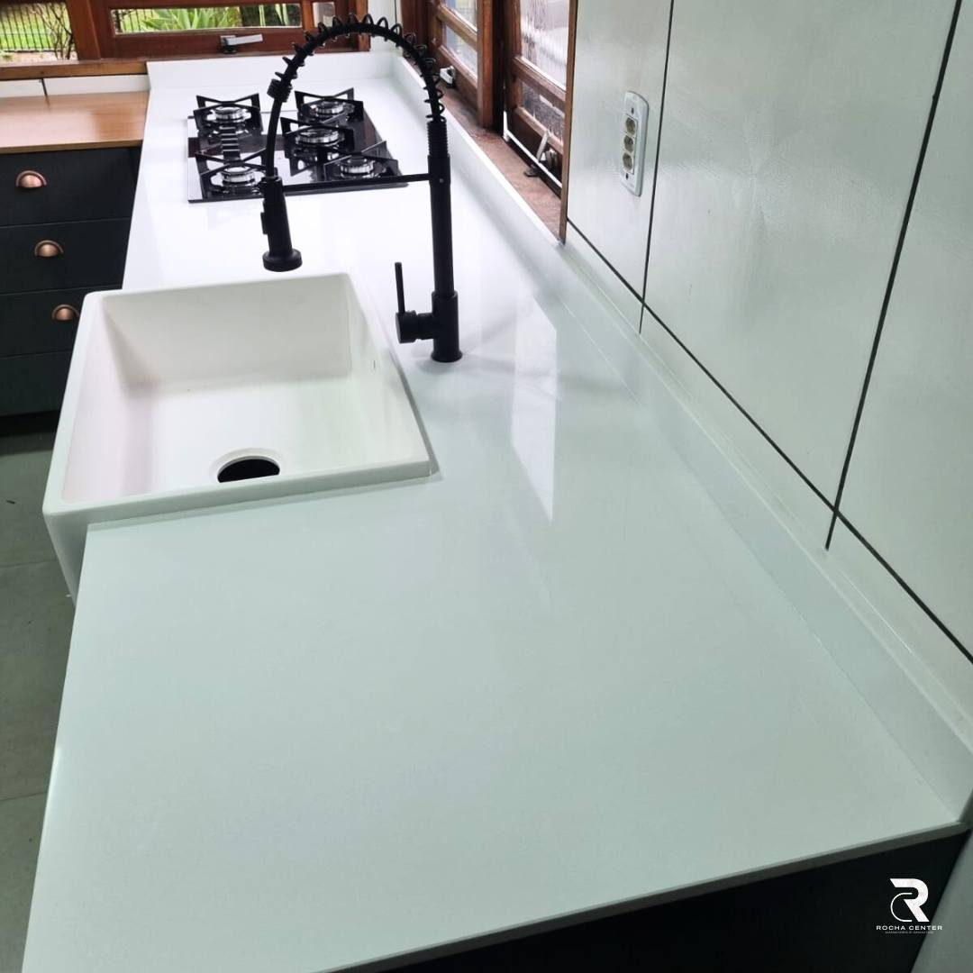 Uma imagem de uma cozinha moderna branca, incluindo bancada, pia, torneira, fogão, armários e janelas